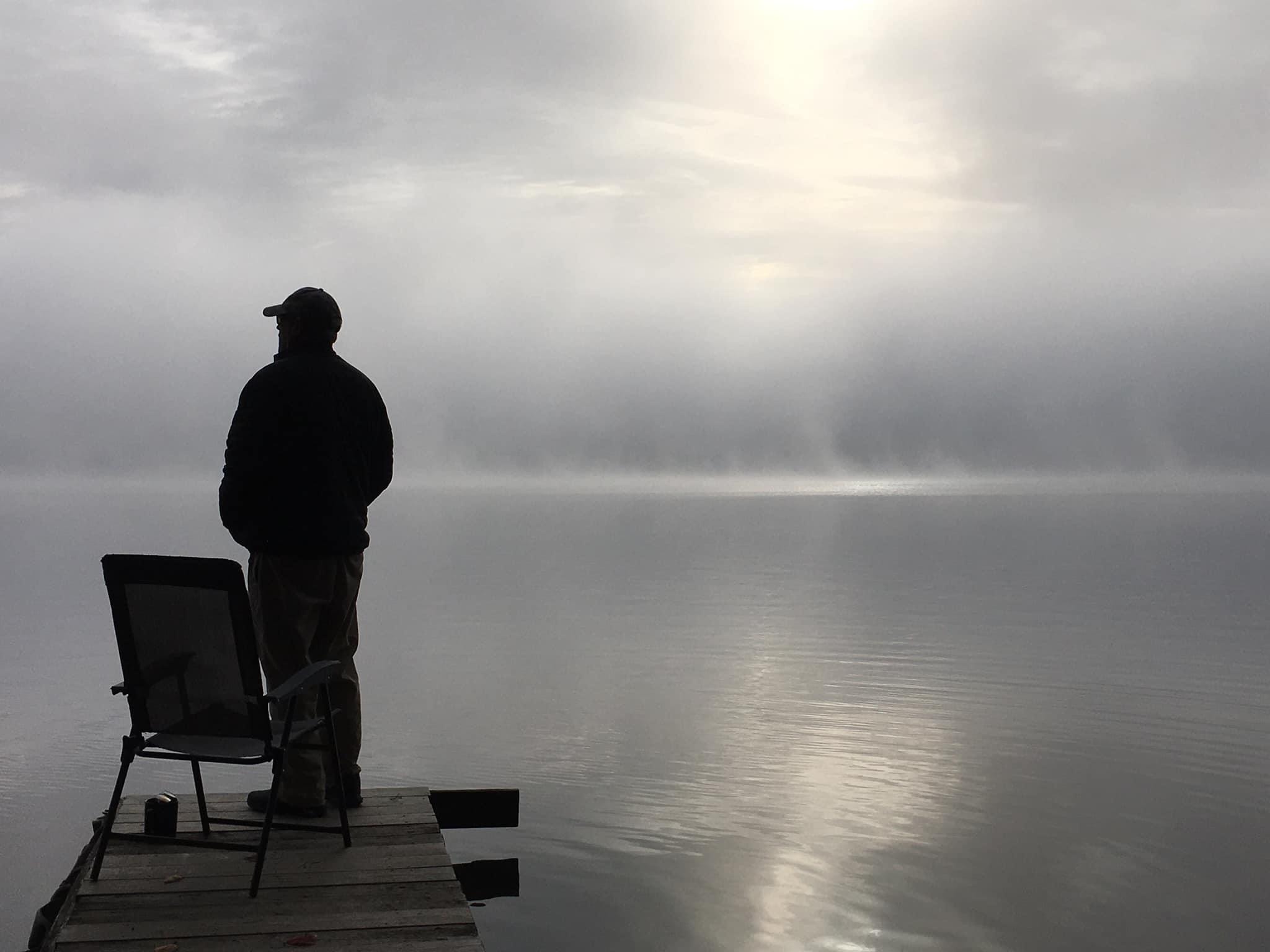Person standing on a dock overlooking calm misty water